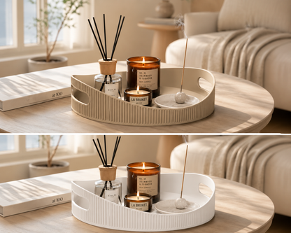 A styled interior scene showing a round light wood coffee table with a beige ribbed tray holding a reed diffuser, two lit candles, and a white incense holder. A matching tray appears below it on the same table, and the background shows a softly blurred sofa and window light.