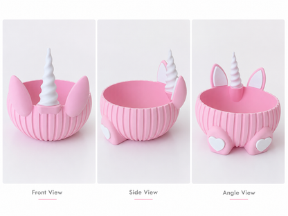 Three views of a pink unicorn-themed bowl on a white background, labeled Front View, Side View, and Angle View. The bowl has a ribbed texture, a white horn, pink ears, and small white heart-shaped feet.