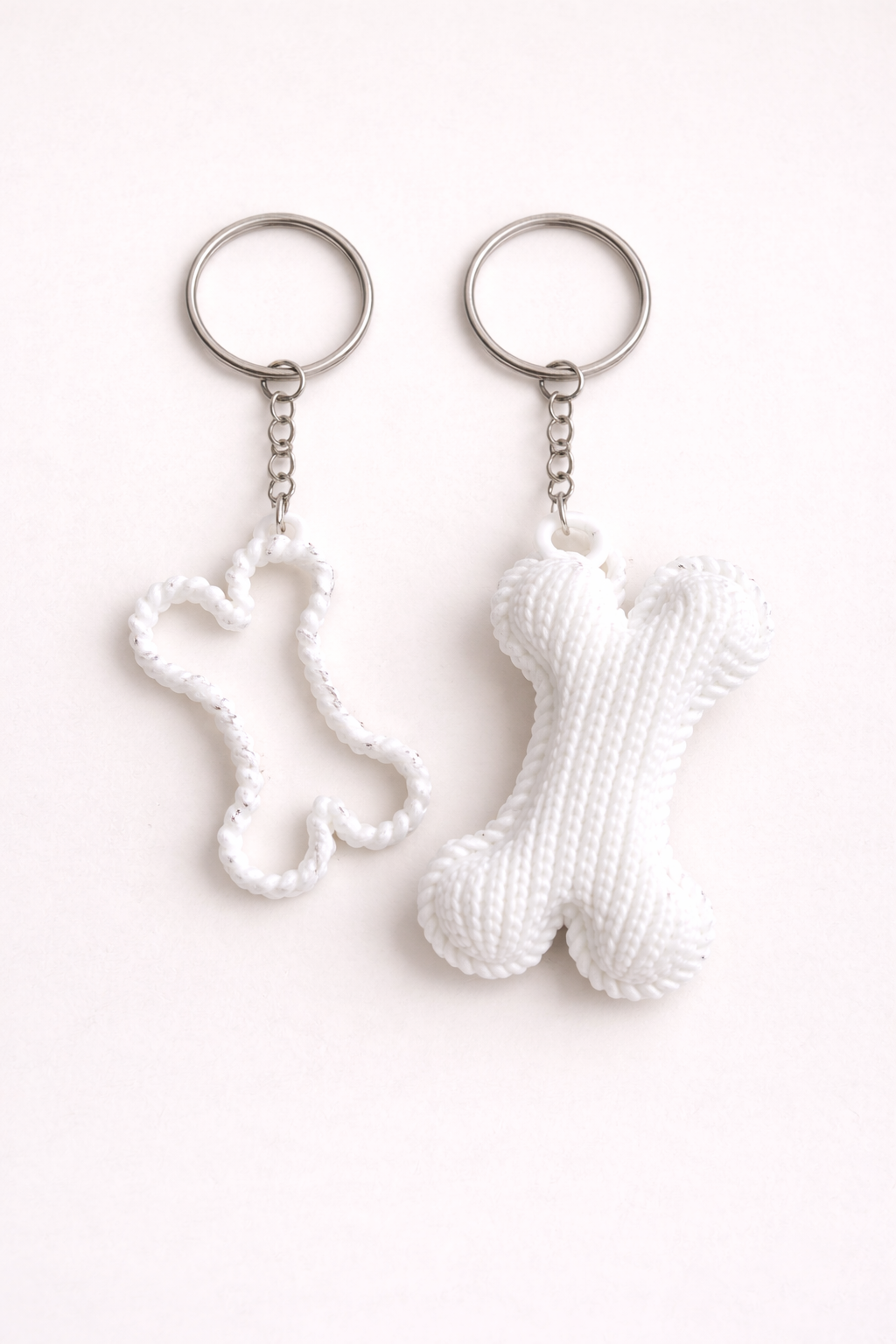 Two white keychains shaped like a sock and a bone on a white background