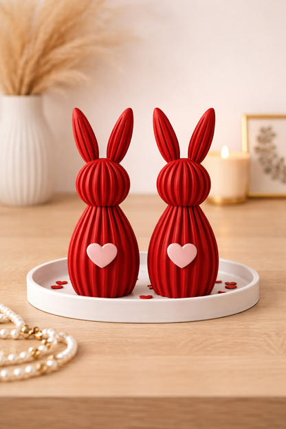 Two red rabbit-shaped decorative items with heart details on a white tray.