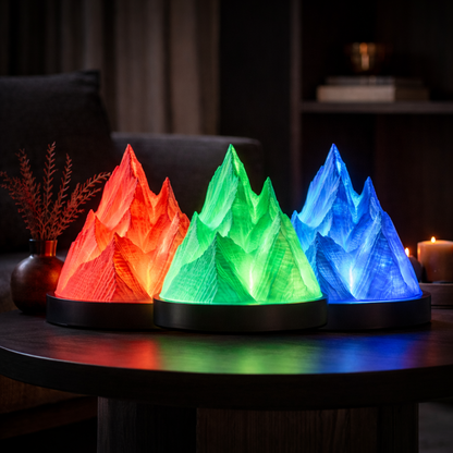 Three mountain-shaped lamps in red, green, and blue on a table with a dark background.