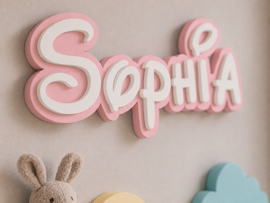 Pink and white 3D wooden name sign spelling 'Sophia' mounted on a beige wall, with a small plush bunny and pastel decor partially visible below.