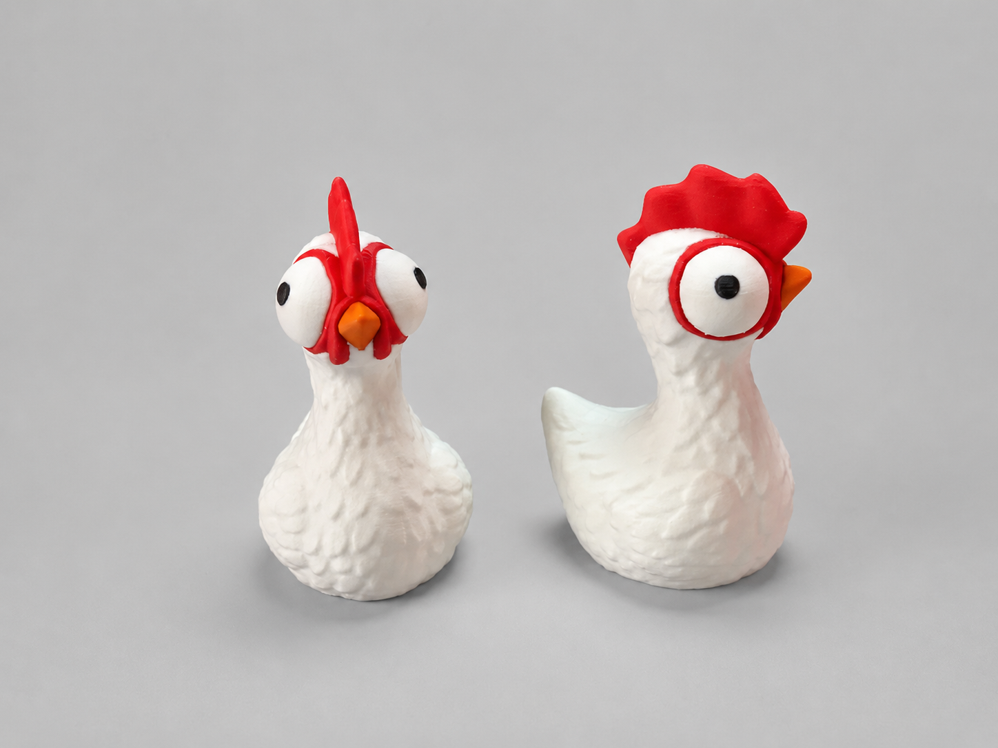 Two ceramic chicken figurines with red combs on a gray background