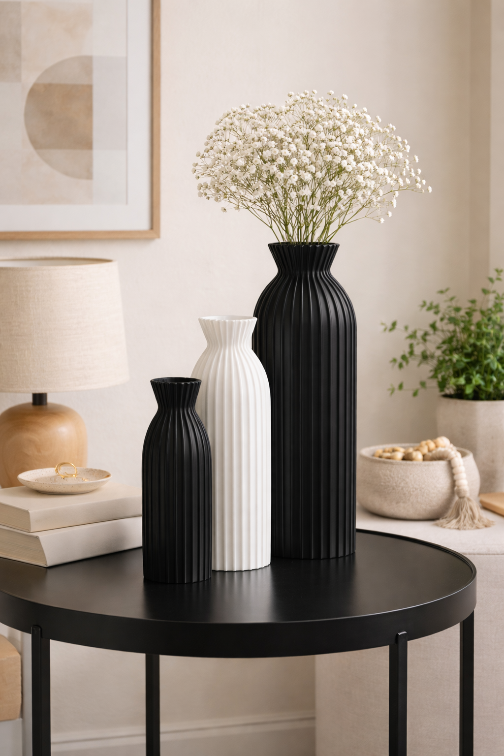 Black and white vases on a round black table with a lamp and decor items in a room.
