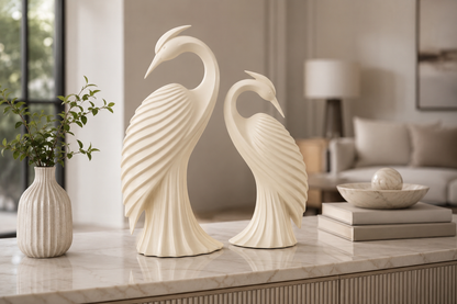 Two cream-colored decorative swan figurines displayed on a marble console table in a modern, softly lit living room setting.