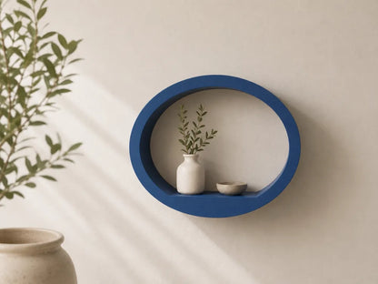 A blue oval floating wall shelf mounted on a beige wall, styled with a small white vase holding green stems and a small bowl. A potted plant is partially visible on the left side with soft diagonal shadows cast across the wall.