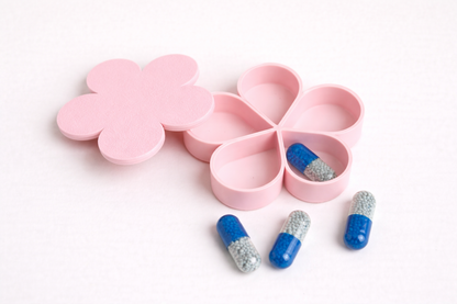 Pink flower-shaped pill organizer with blue and silver capsules on a white background