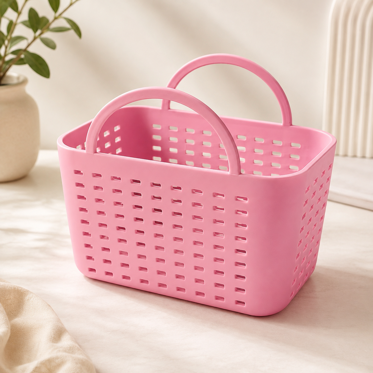 A pink plastic storage basket with two loop handles, shown on a light beige fabric surface with a neutral indoor background.