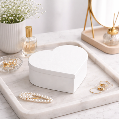 Heart-shaped white jewelry box on a marble surface with pearls and a perfume bottle.