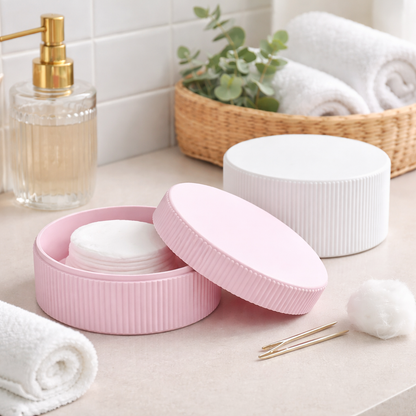 Pink and white ceramic containers on a bathroom counter with cotton pads and towels.