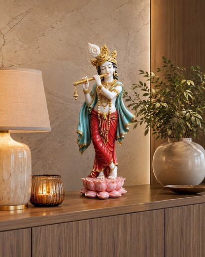 A decorative statue of a seated Hindu deity on a pink lotus base, styled on a wooden cabinet in a warm interior setting with a lamp, candle holder, and potted plant.