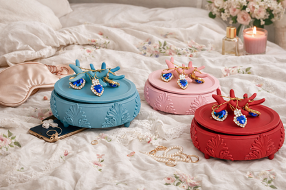 Three decorative jewelry boxes in blue, pink, and red with matching earrings on a floral bedspread.