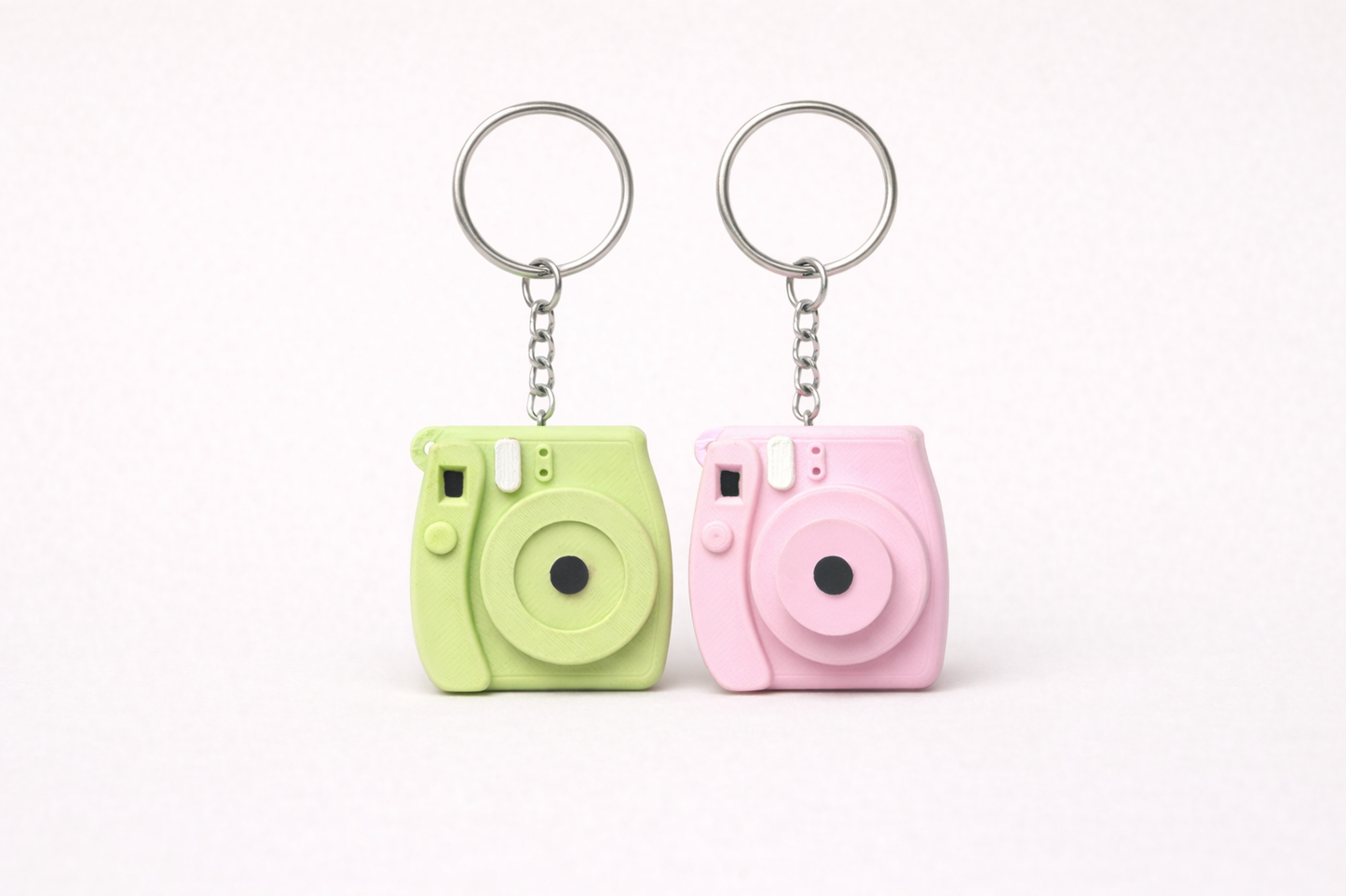 Two camera-shaped keychains, one green and one pink, on a white background.
