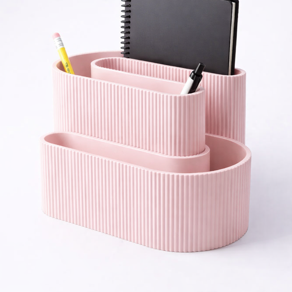 Pink ribbed desk organizer with stationery items on a white background
