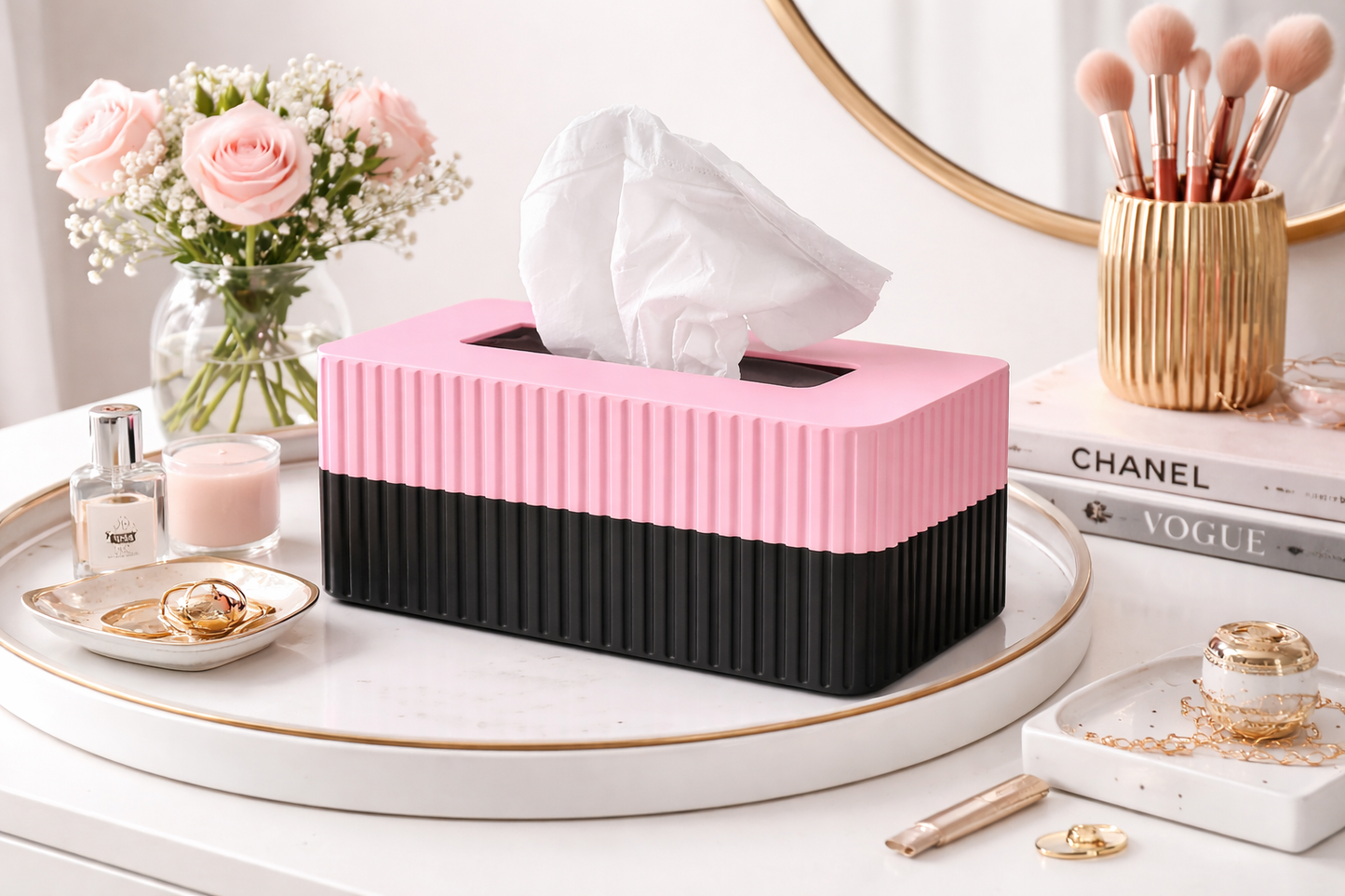 Pink and black tissue box on a vanity table with makeup and decor items.