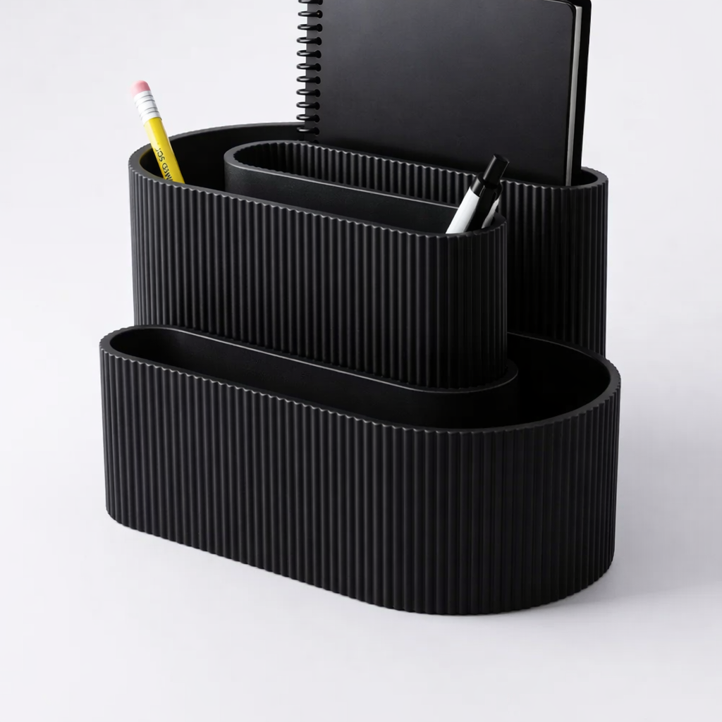 Black ribbed desk organizer with stationery items on a light gray background
