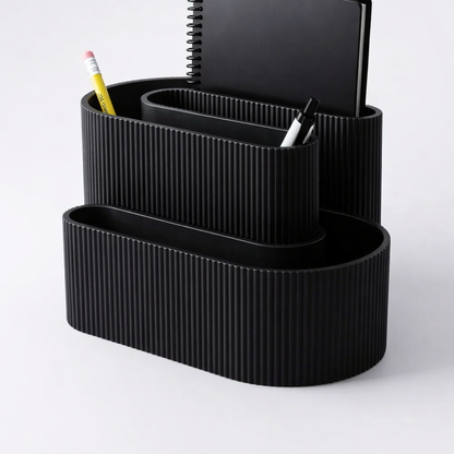 Black ribbed desk organizer with stationery items on a light gray background
