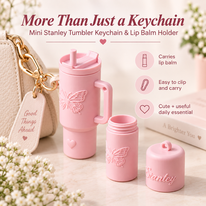A pink mini Stanley tumbler keychain and lip balm holder set shown on a light tabletop with decorative flowers and a handbag. The set includes a handled tumbler with a butterfly embossing, an open tumbler base, a separate lip balm container, and a small cap embossed with the name Stanley.