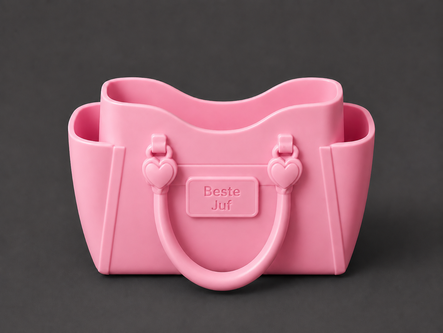 A pink silicone handbag-shaped container with heart-shaped handles and a central embossed label reading 'Beste Juf', shown on a dark gray background.
