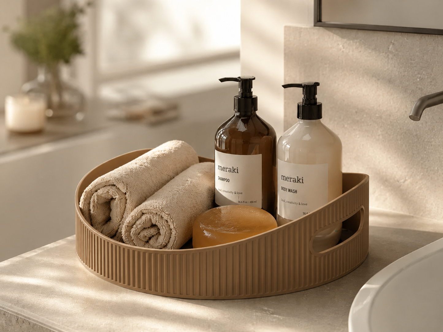 A round ribbed beige bathroom organizer tray holding two rolled towels, a bar of soap, and two pump bottles on a bathroom counter.