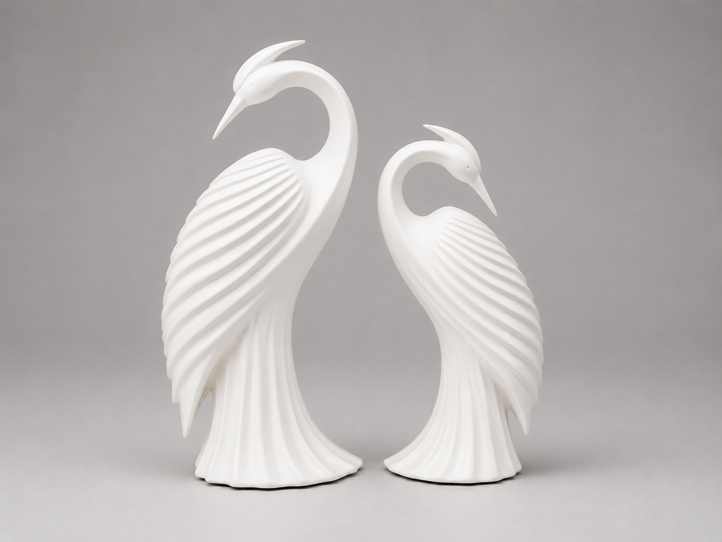 A pair of white ceramic decorative bird sculptures shaped like stylized herons or cranes, standing side by side against a neutral gray studio background.