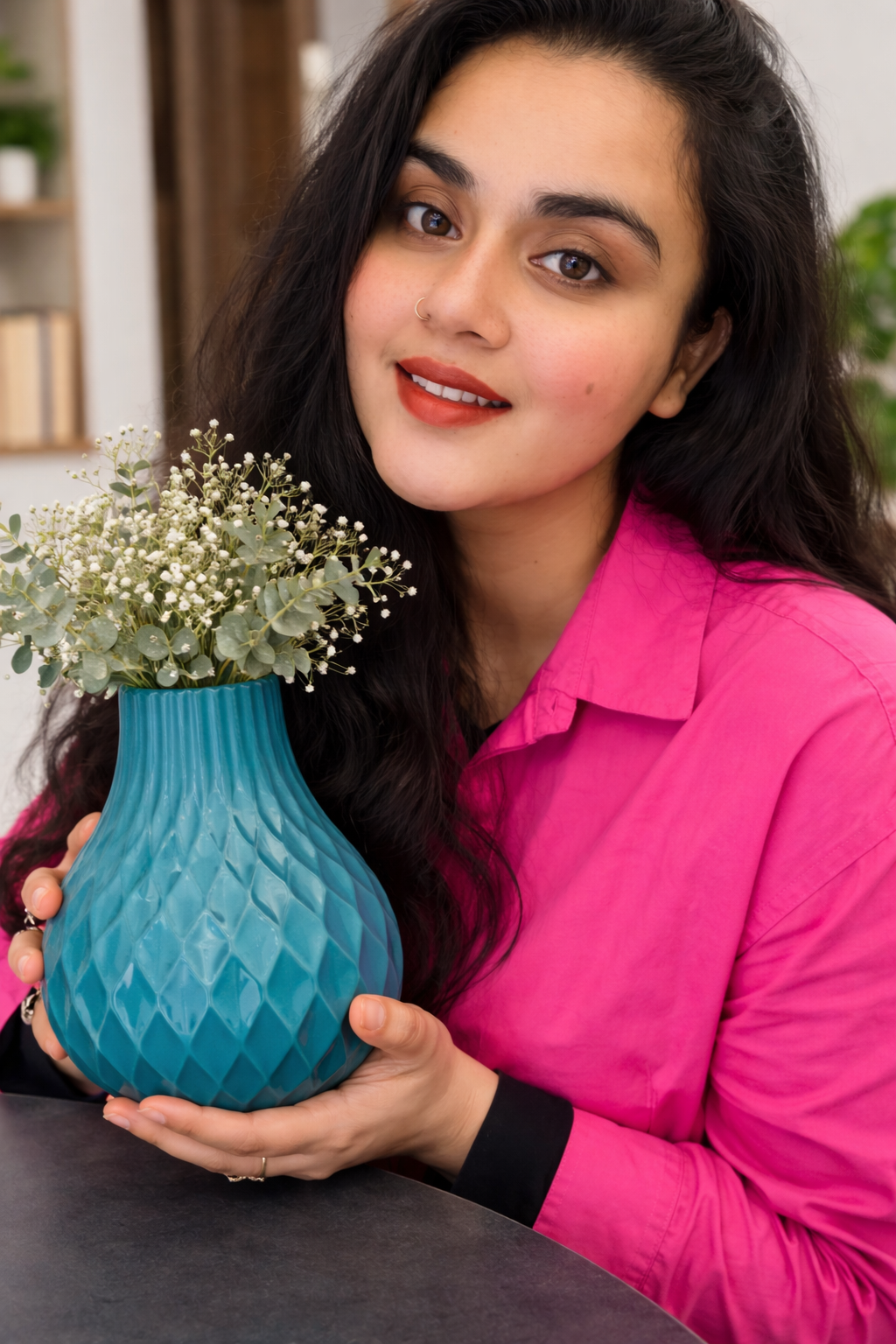 Woman holding a blue textured vase with a plant, wearing a pink shirt.