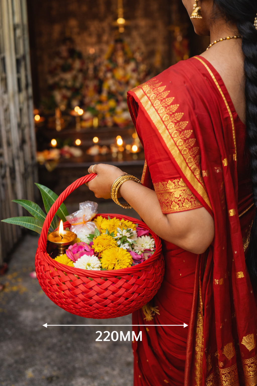 Person in a red saree holding a red basket with flowers and a candle, with a blurred background.