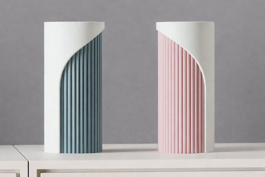 Two modern vases, one gray and one pink, on a white surface with a gray background.