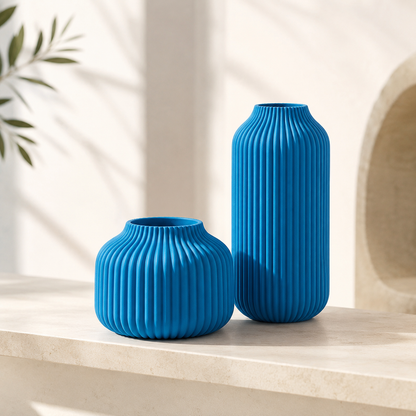 Two ribbed ceramic vases in bright blue, one short and rounded and one tall and slender, displayed on a light stone surface with soft shadow overlays.