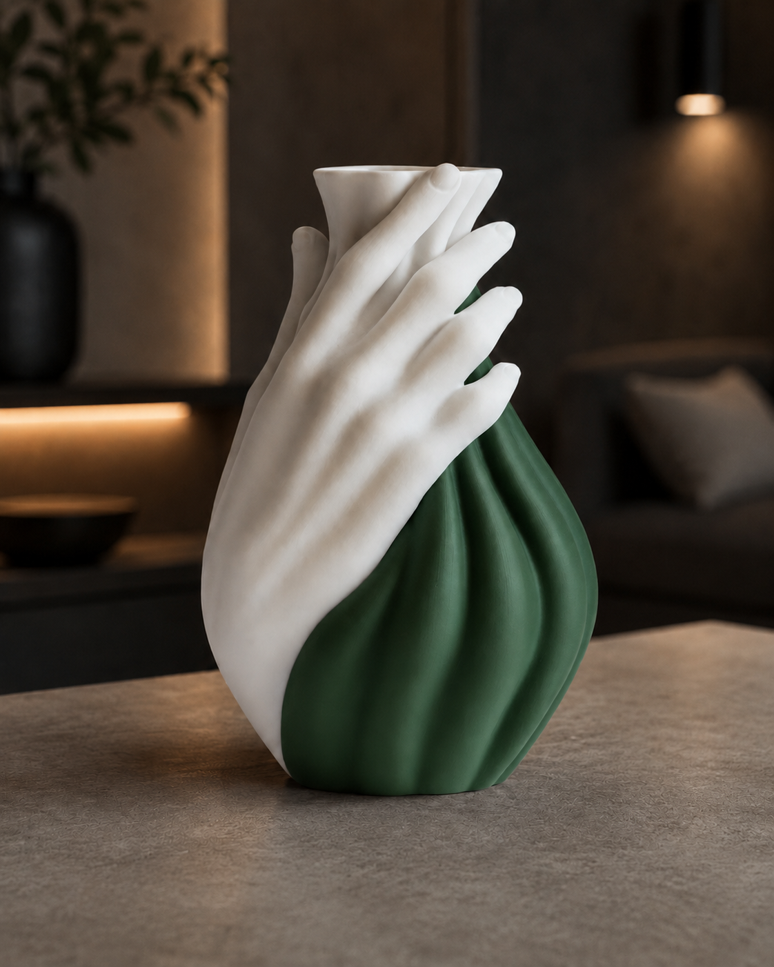 A sculptural ceramic vase shaped like a hand, with one half in matte white and the other in deep green, displayed on a stone tabletop in a softly lit modern interior.