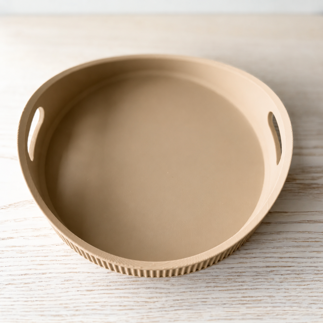 A round beige tray with integrated side handles and a ribbed outer edge, photographed on a light wood surface.
