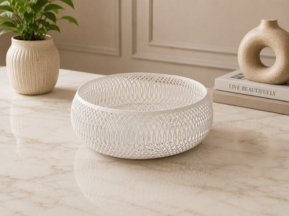 A round white ceramic bowl with an intricate openwork lattice pattern, displayed on a light marble tabletop in a styled interior setting.