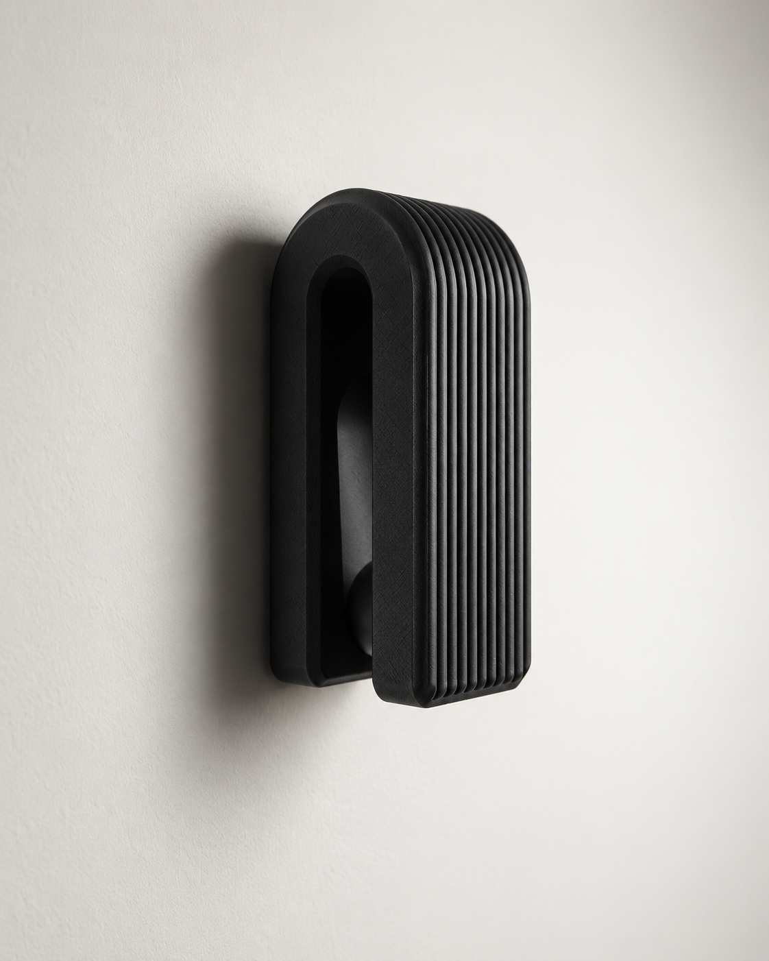 A modern black wall-mounted light fixture with a ribbed, vertically grooved rectangular design, shown mounted on a plain off-white wall.