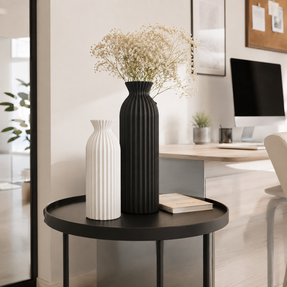 Two ribbed ceramic vases, one black and one white, displayed on a black round side table in a modern home office setting.