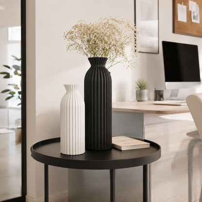 Two ribbed ceramic vases, one black and one white, displayed on a black round side table in a modern home office setting.