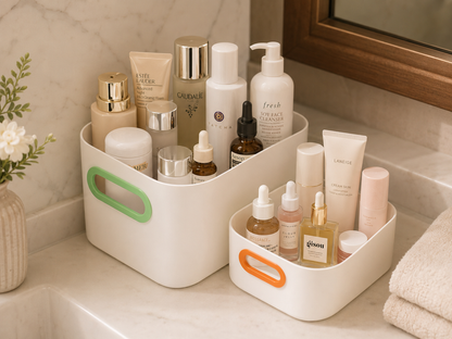 Two white plastic bathroom organizer bins with colorful handles, filled with skincare and cosmetic bottles, set on a marble bathroom counter.