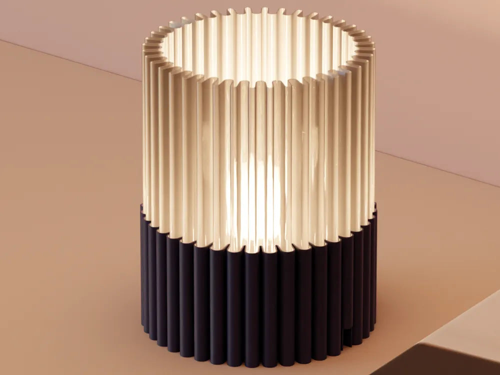 A modern cylindrical table lamp with a fluted shade, featuring a warm cream upper section and a dark navy lower section, shown lit on a beige surface.