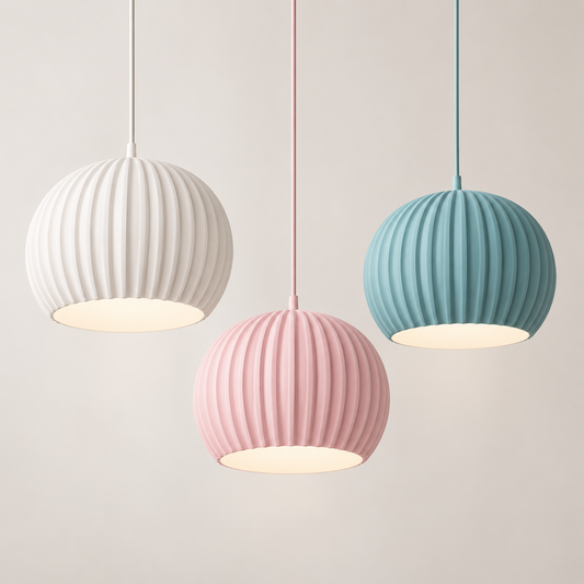 Three ribbed spherical pendant lights in white, pink, and teal-blue hang against a plain light beige wall, each glowing with a warm light from the open bottom.