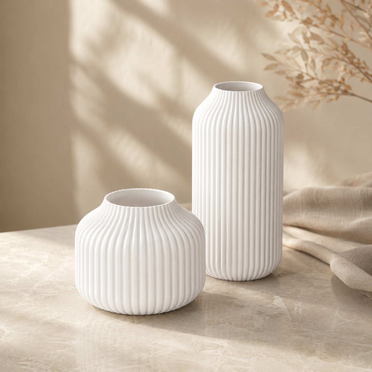 Two white ribbed ceramic vases, one small and one tall, displayed on a beige stone surface with soft natural shadows and dried floral decor in the background.