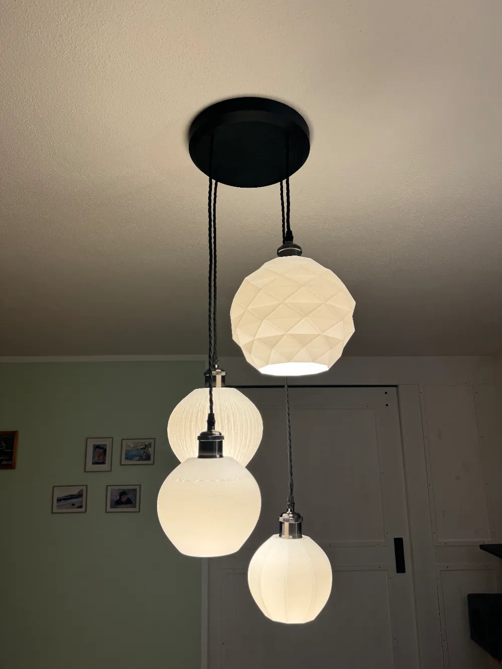 A three-light pendant ceiling fixture with a black round canopy, black cords, and three white textured globe shades hanging in a home interior.