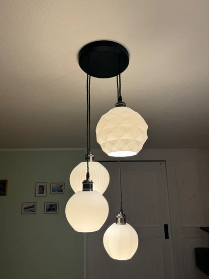 A three-light pendant ceiling fixture with a black round canopy, black cords, and three white textured globe shades hanging in a home interior.