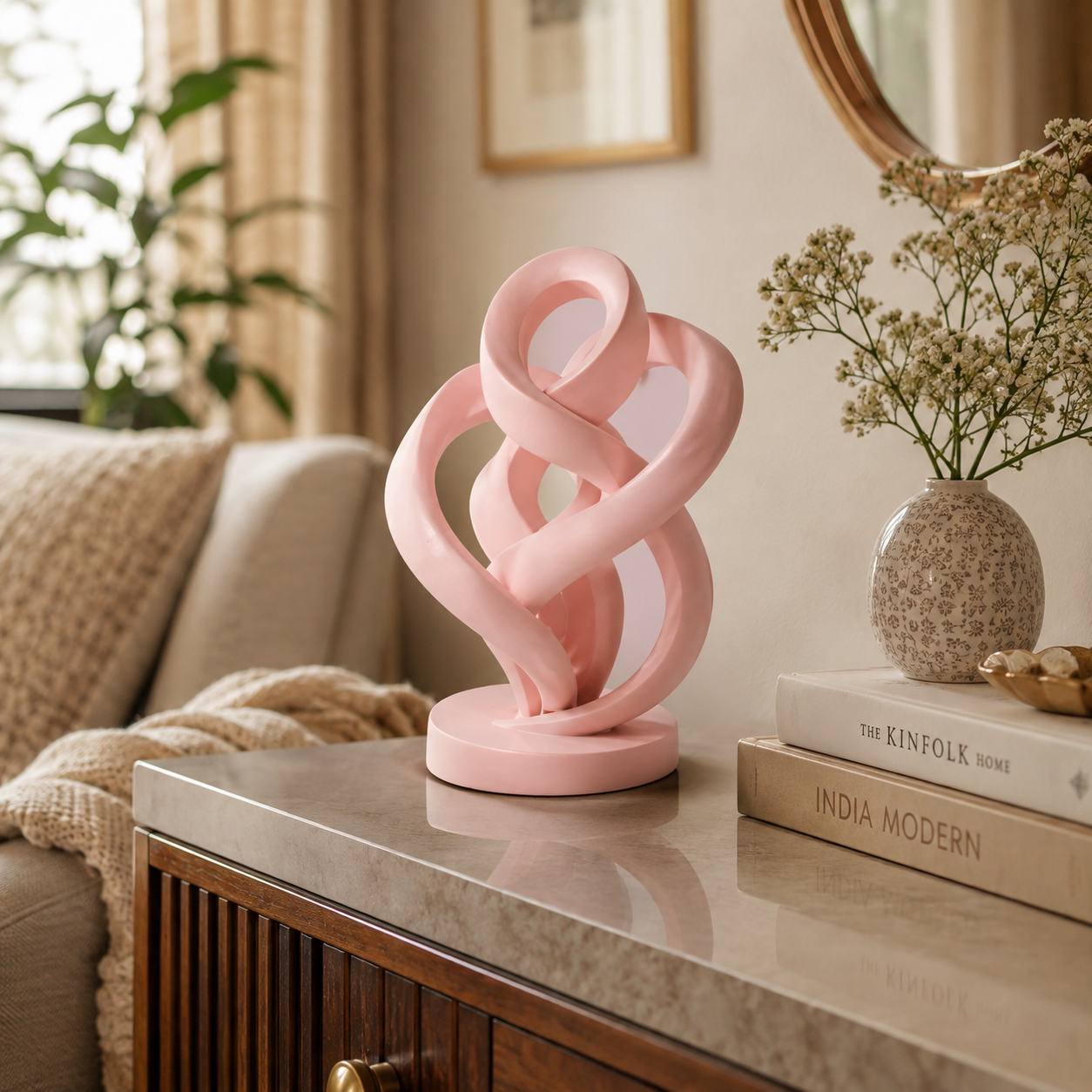 A pink abstract sculptural table lamp with interlocking curved loops sits on a marble-top console table in a styled living room setting.