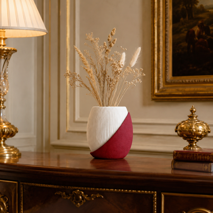 A modern ceramic vase with a diagonal split design in white and deep red, filled with dried grasses, displayed on an ornate dark wood console table in a classic room setting.