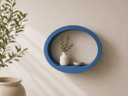 A blue oval floating wall shelf mounted on a beige wall, styled with a small white ceramic vase and a dried green plant, with a beige ceramic pot partially visible in the foreground.