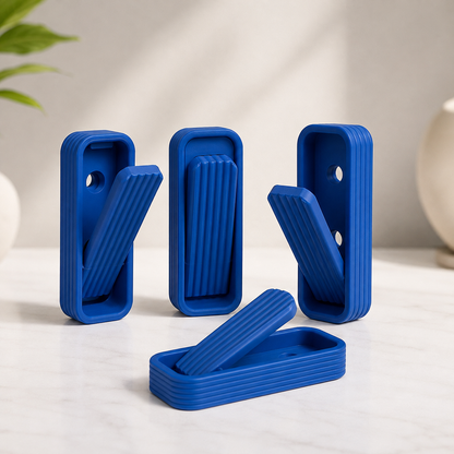 Four blue rectangular silicone or plastic clips with ribbed sides and hinged flaps, arranged on a light marble-like surface against a soft neutral background.