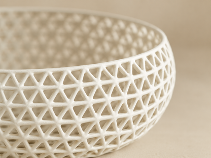 A close-up of a white ceramic bowl with an intricate open geometric lattice pattern, set against a warm beige background.
