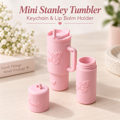 A pink mini Stanley tumbler shown in three views on a light wood surface: one assembled with lid and handle, one open bottle, and one cap. The tumbler has an embossed butterfly and heart design.