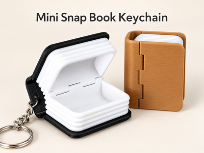 Two mini snap book keychains shown on a light beige background with the text 'Mini Snap Book Keychain' at the top. One keychain is open, showing white lined pages with a black cover and attached silver key ring.