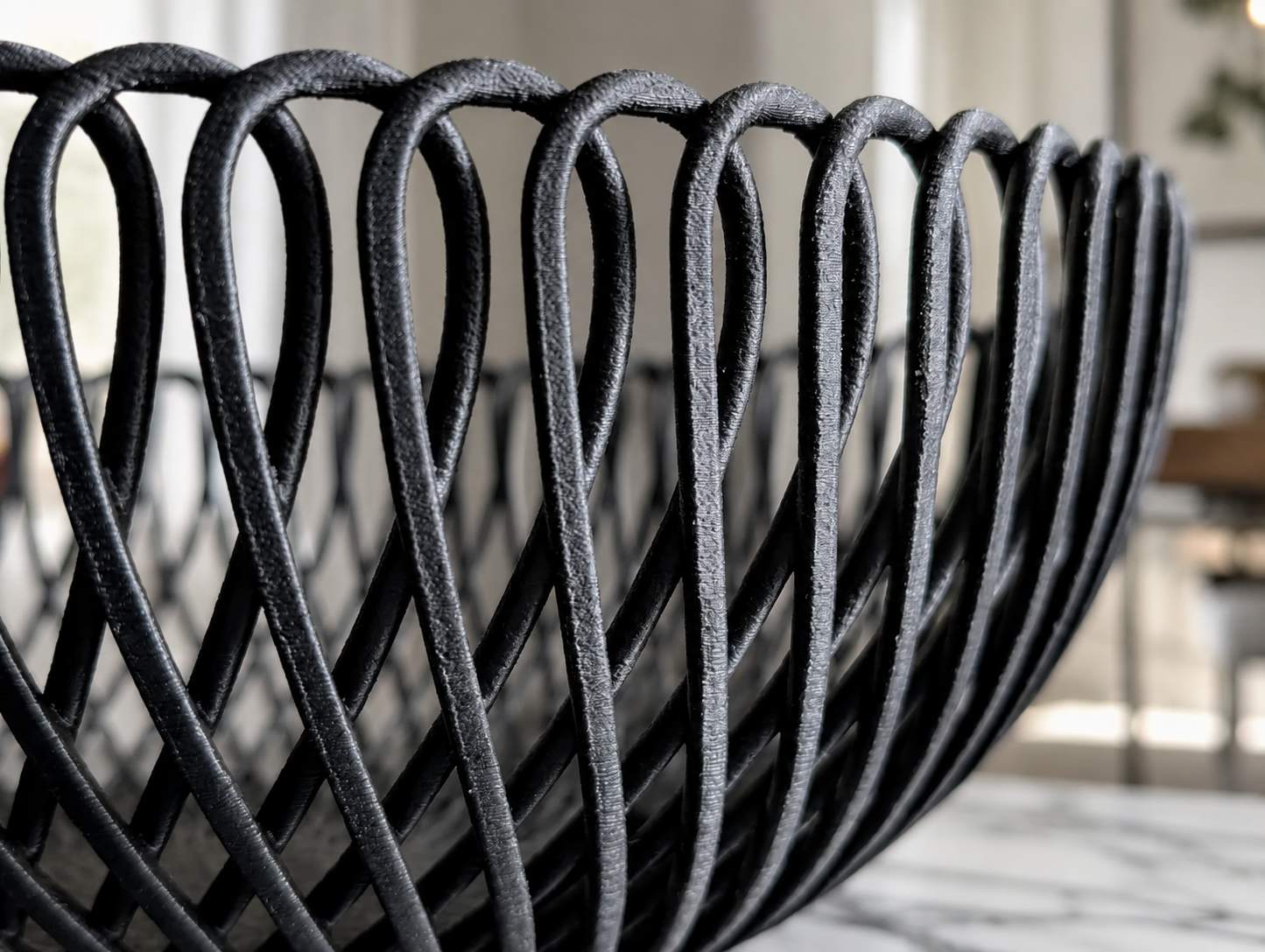 Close-up of a black woven basket or bowl with a textured finish, set against a softly blurred indoor background.
