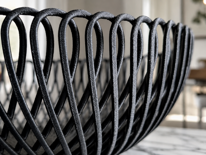 Close-up of a black woven basket or bowl with a textured finish, set against a softly blurred indoor background.
